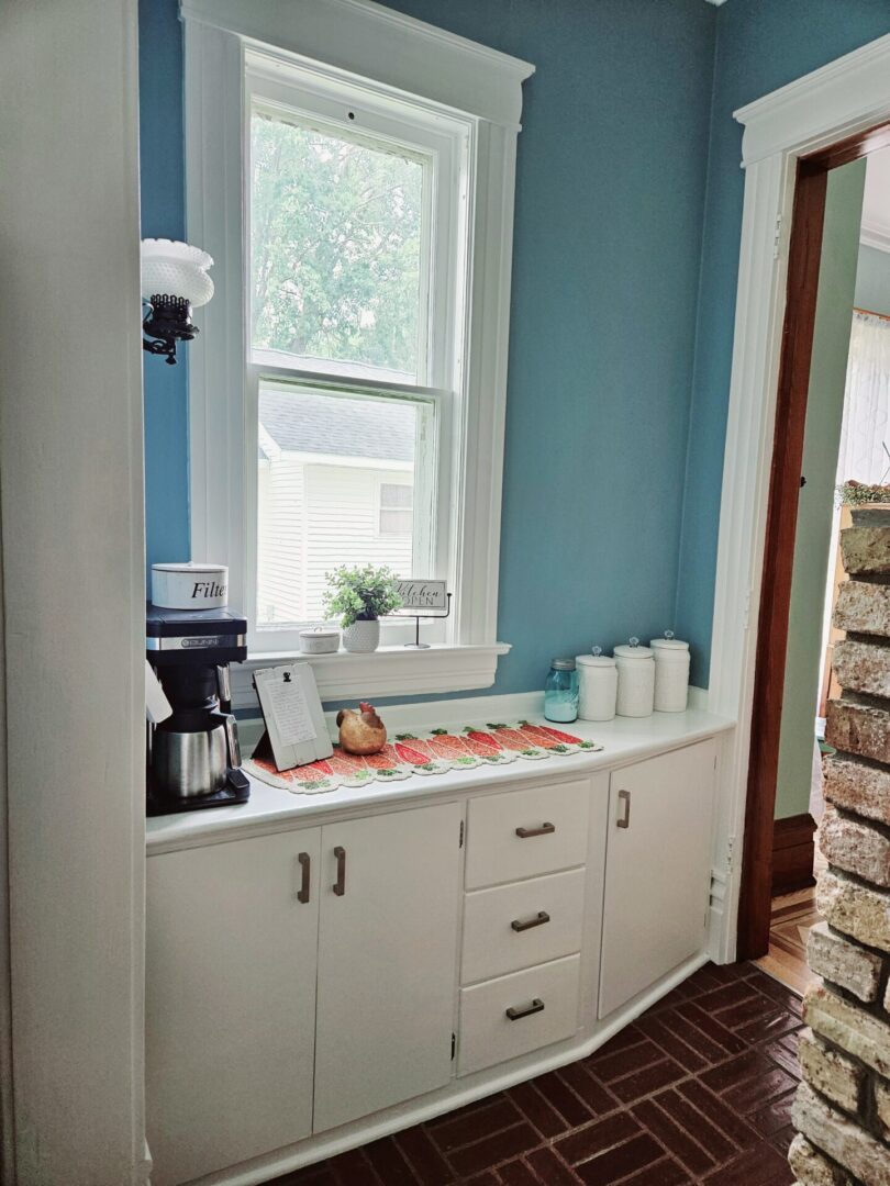 A kitchen with blue walls and white cupboards.