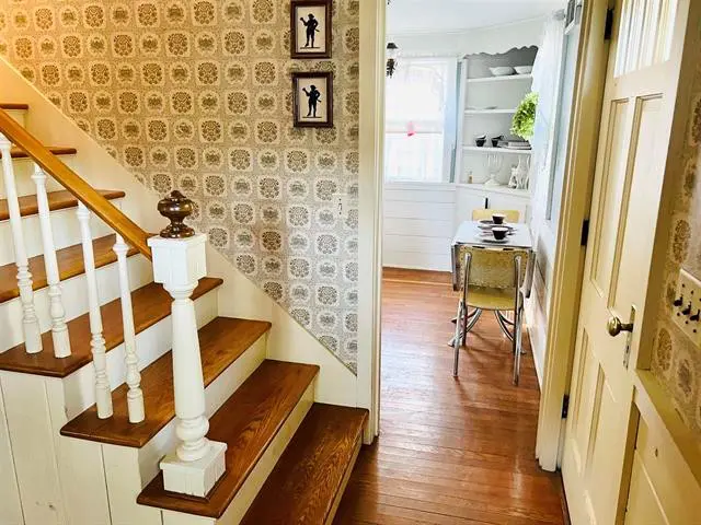 A hallway with wooden floors and white stairs.